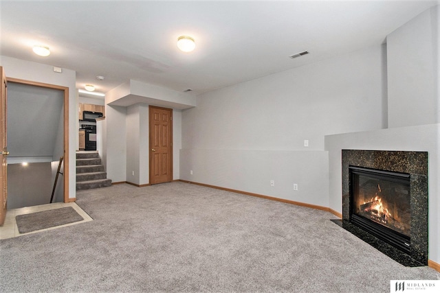 unfurnished living room featuring stairway, carpet, baseboards, and a high end fireplace