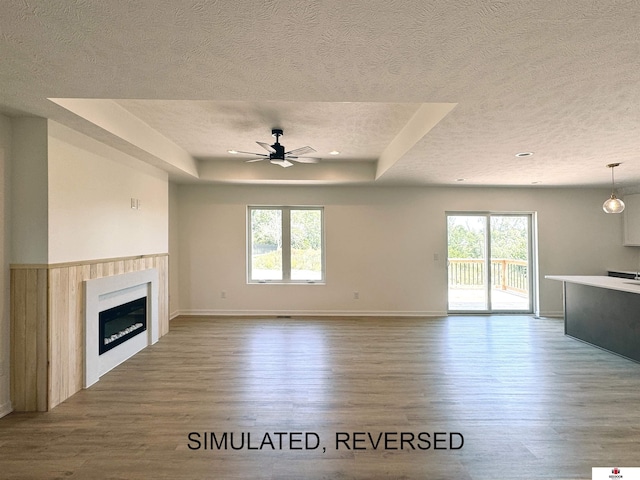 unfurnished living room with a tray ceiling, plenty of natural light, a textured ceiling, and wood finished floors