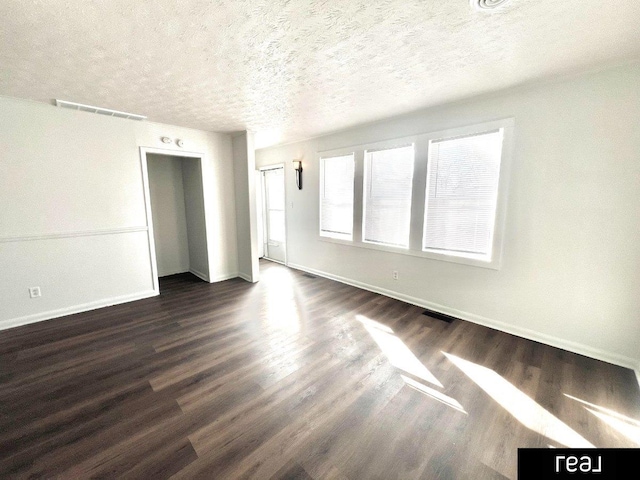 empty room with visible vents, a textured ceiling, dark wood-type flooring, and baseboards