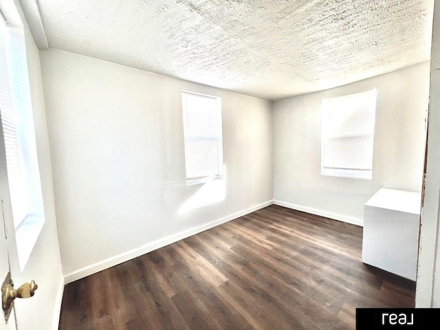 spare room with baseboards, a textured ceiling, and dark wood finished floors