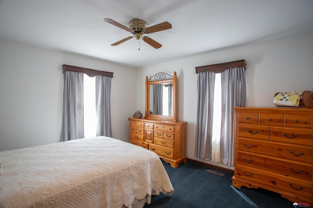 bedroom featuring multiple windows, visible vents, dark colored carpet, and ceiling fan