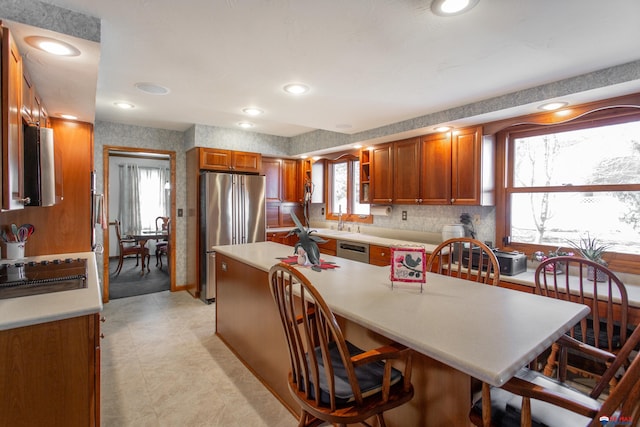 kitchen with wallpapered walls, stainless steel appliances, brown cabinetry, and light countertops