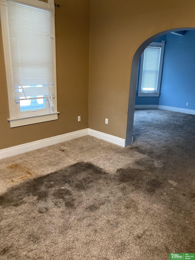 carpeted empty room with plenty of natural light, baseboards, and arched walkways