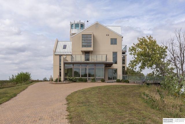 view of front of home featuring a balcony, a standing seam roof, stucco siding, a front lawn, and metal roof