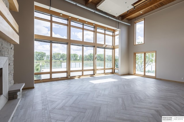 unfurnished living room featuring a stone fireplace, baseboards, and a towering ceiling