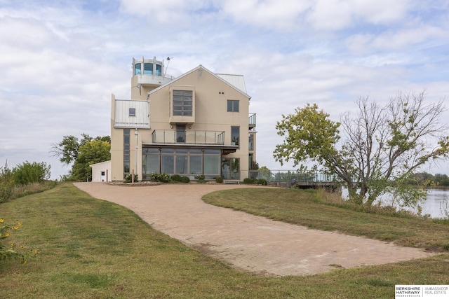 back of property featuring a balcony, driveway, a yard, and stucco siding