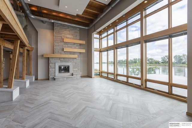 unfurnished living room with a stone fireplace, a high ceiling, baseboards, and a water view