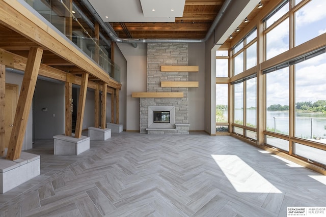 unfurnished living room with baseboards, a water view, a high ceiling, and a stone fireplace