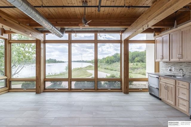 unfurnished sunroom with a water view, beamed ceiling, wooden ceiling, a ceiling fan, and a sink