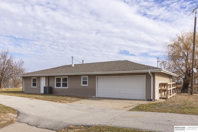 ranch-style home with driveway, roof with shingles, central AC unit, and an attached garage