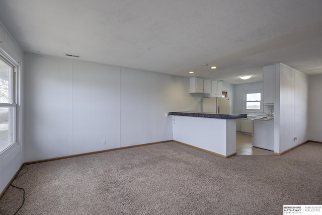 kitchen featuring visible vents, freestanding refrigerator, a peninsula, range, and light colored carpet