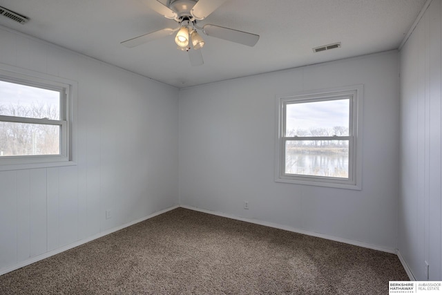 carpeted spare room with a wealth of natural light, visible vents, and ceiling fan