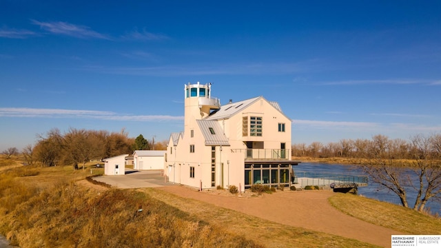 exterior space with stucco siding, metal roof, a balcony, and a water view