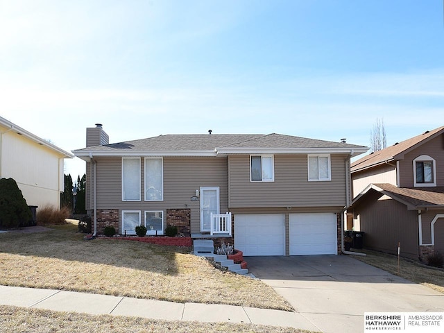 raised ranch with a front lawn, concrete driveway, an attached garage, brick siding, and a chimney