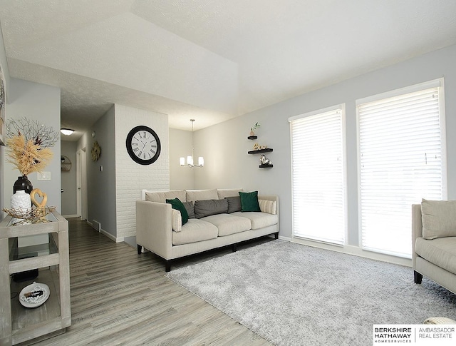 living area with a chandelier, baseboards, a textured ceiling, and light wood-style flooring