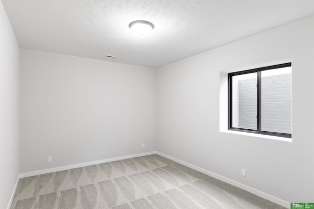 spare room featuring visible vents, baseboards, light colored carpet, and a textured ceiling