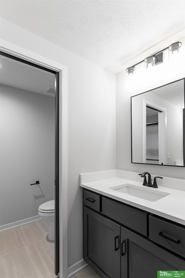 bathroom with baseboards, toilet, vanity, and a textured ceiling