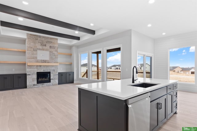 kitchen featuring beam ceiling, a sink, light wood-style floors, a stone fireplace, and dishwasher