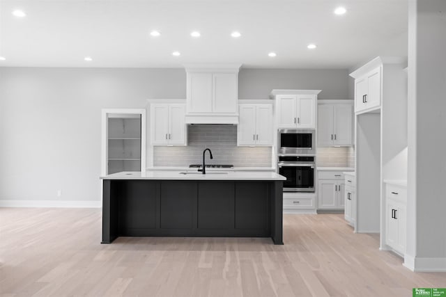 kitchen with a kitchen island with sink, a sink, light countertops, white cabinetry, and stainless steel microwave