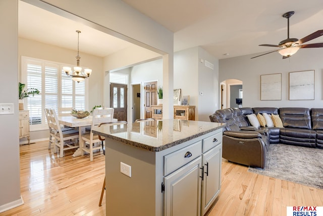 kitchen with light wood-type flooring, light stone counters, open floor plan, a center island, and arched walkways