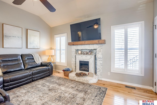 living area featuring wood finished floors, visible vents, baseboards, lofted ceiling, and a fireplace