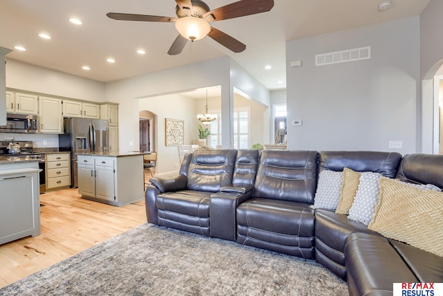 living room featuring visible vents, light wood-type flooring, ceiling fan with notable chandelier, recessed lighting, and arched walkways