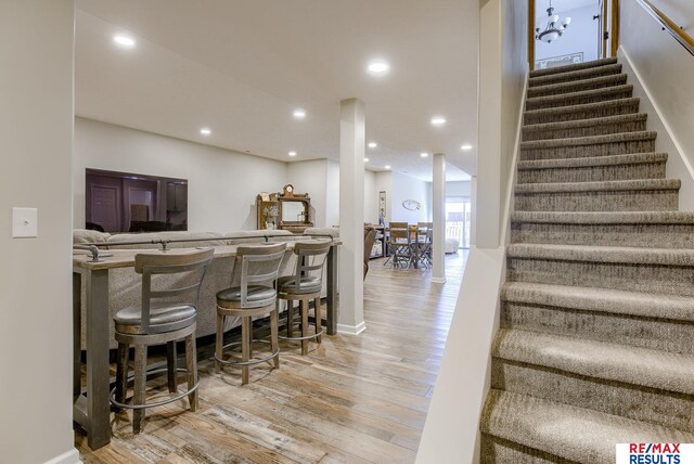 bar with stairs, a bar, recessed lighting, and wood finished floors