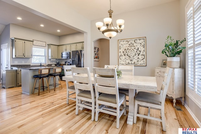 dining space with recessed lighting, arched walkways, an inviting chandelier, and light wood finished floors