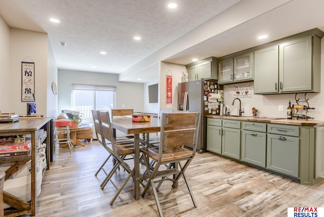 kitchen featuring stainless steel refrigerator with ice dispenser, a sink, recessed lighting, light wood-style floors, and green cabinets