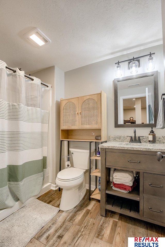 bathroom with toilet, vanity, a shower with curtain, wood finished floors, and a textured ceiling