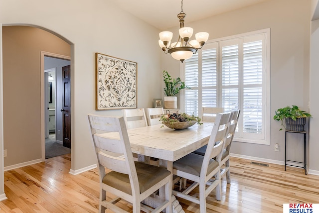 dining area with an inviting chandelier, light wood-style flooring, baseboards, and arched walkways