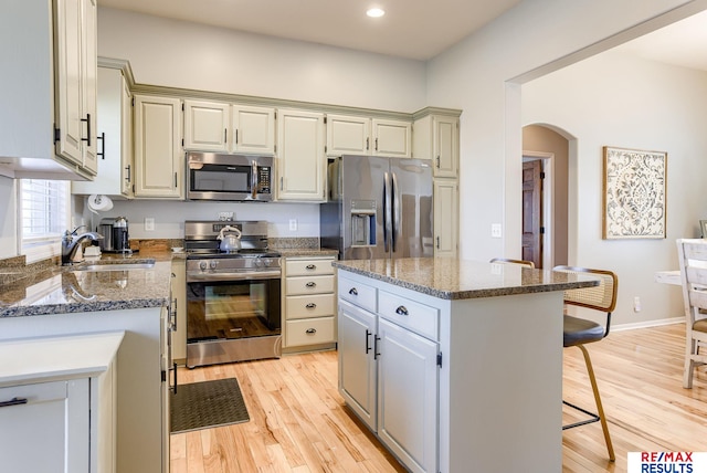 kitchen featuring arched walkways, a sink, appliances with stainless steel finishes, a kitchen breakfast bar, and light wood-type flooring