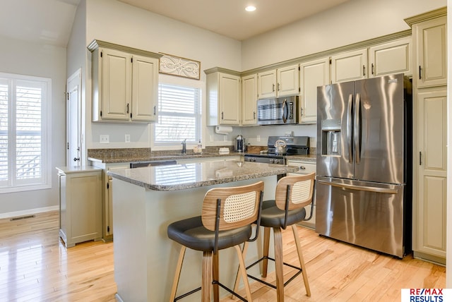 kitchen featuring a kitchen island, a breakfast bar, light wood-style floors, stainless steel appliances, and a sink