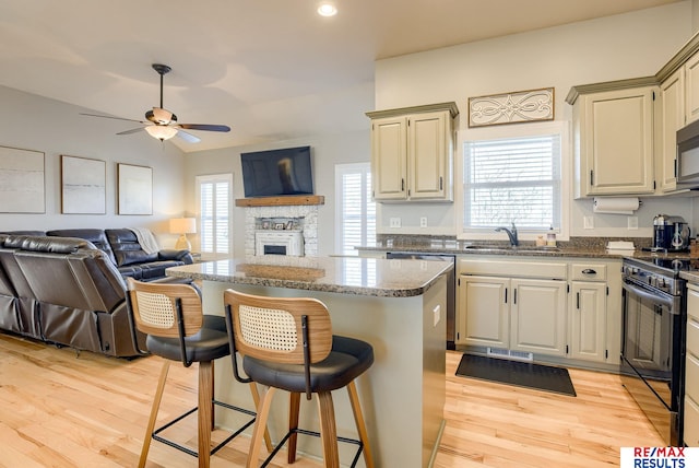 kitchen with dark stone counters, a sink, black range with electric stovetop, open floor plan, and a center island