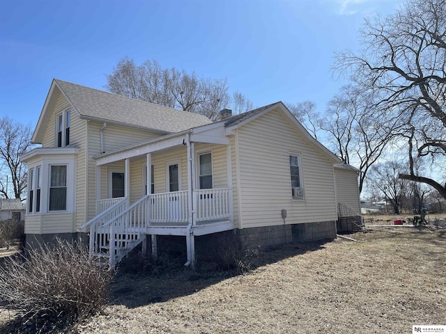 exterior space featuring a porch, a chimney, and a shingled roof