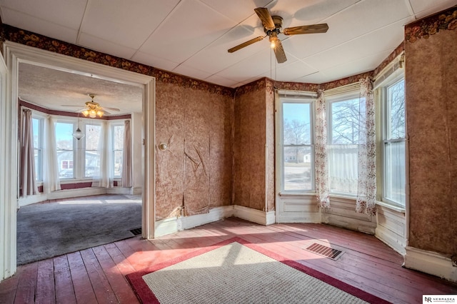 empty room featuring visible vents, wood-type flooring, baseboards, and ceiling fan