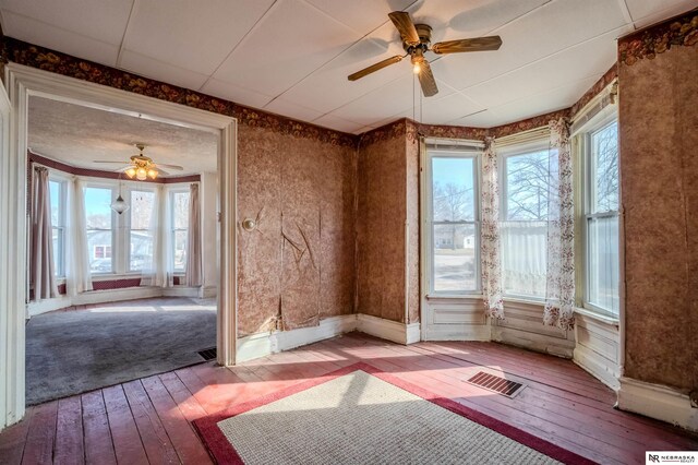 empty room featuring visible vents, wood-type flooring, baseboards, and ceiling fan