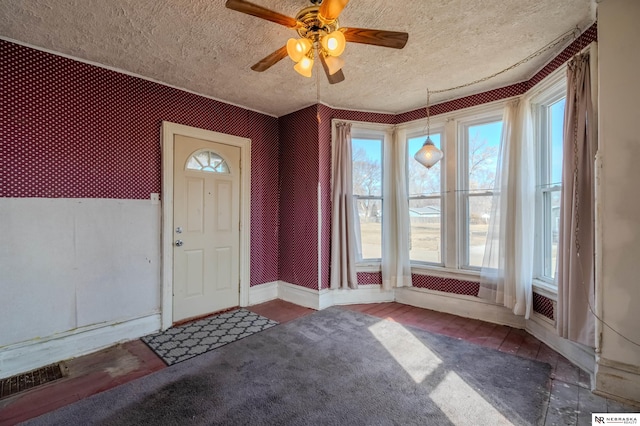 foyer with visible vents, a textured ceiling, wallpapered walls, baseboards, and ceiling fan