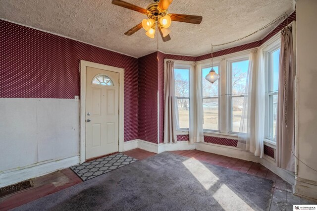 foyer with visible vents, a textured ceiling, wallpapered walls, baseboards, and ceiling fan