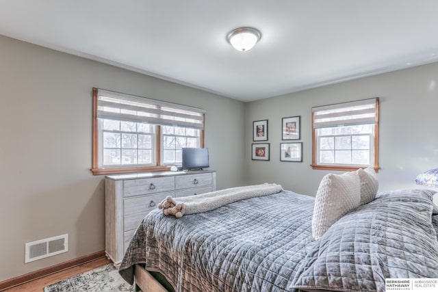 bedroom with visible vents, multiple windows, baseboards, and wood finished floors