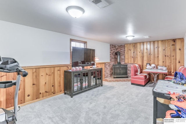 living room featuring visible vents, a wainscoted wall, carpet floors, wood walls, and a wood stove