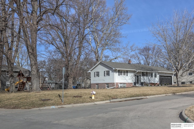 view of front facade with brick siding, an attached garage, a chimney, and a front yard