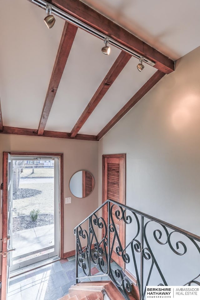 entrance foyer with track lighting, stone finish floor, vaulted ceiling with beams, and baseboards