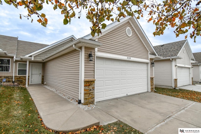 view of side of home with stone siding, an attached garage, and concrete driveway