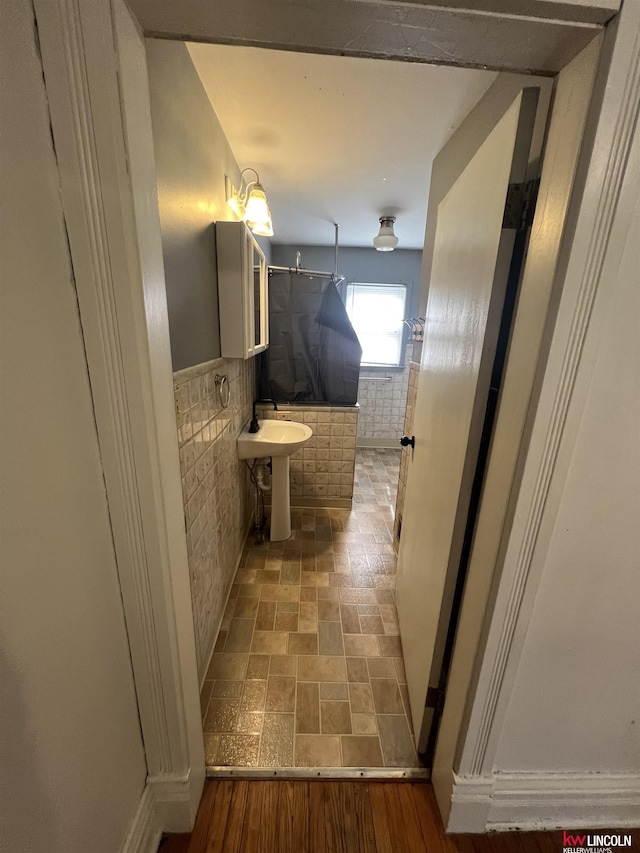 bathroom with a sink, stone finish flooring, tile walls, wainscoting, and walk in shower