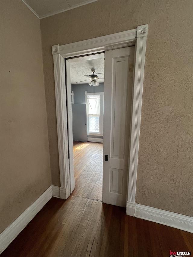 hallway with a textured wall, crown molding, baseboards, and hardwood / wood-style flooring