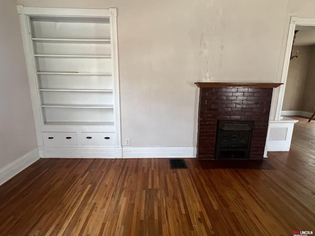 unfurnished living room featuring visible vents, a brick fireplace, baseboards, built in features, and wood finished floors