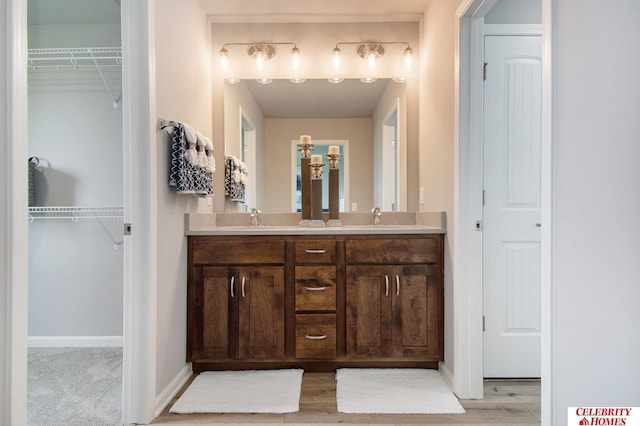 bathroom featuring double vanity, a spacious closet, baseboards, and a sink