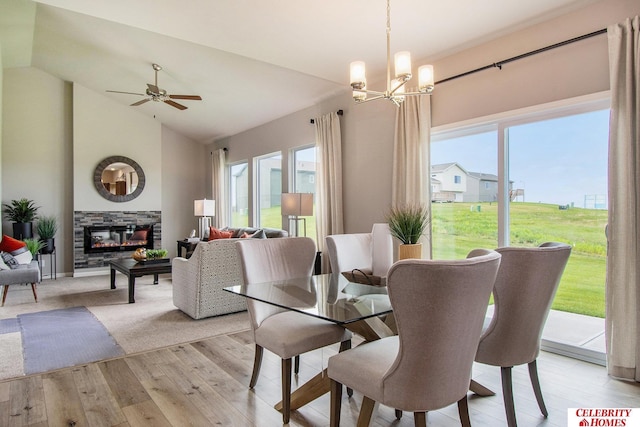 dining space with light wood-type flooring, plenty of natural light, a fireplace, and ceiling fan with notable chandelier