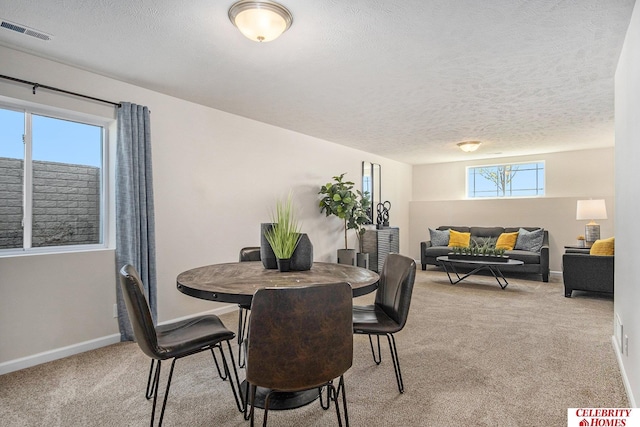 dining room with a textured ceiling, baseboards, visible vents, and light carpet